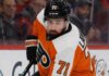 Detroit Red Wings captain Dylan Larkin wearing a Philadelphia Flyers home uniform and orange helmet in a hockey pose, illustrating recent NHL trade rumors linking him to Philly.