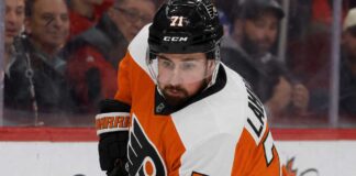 Detroit Red Wings captain Dylan Larkin wearing a Philadelphia Flyers home uniform and orange helmet in a hockey pose, illustrating recent NHL trade rumors linking him to Philly.