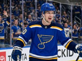 Elias Pettersson Trade Rumors: St. Louis Blues Linked to Vancouver Canucks Center Smiling Elias Pettersson wearing a St. Louis Blues home jersey with Blue Note logo and #40 helmet, celebrating on ice with cheering crowd; speculative trade visualization.