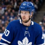 A close-up photograph of Elias Pettersson looking off-camera, wearing an edited blue Toronto Maple Leafs home jersey with the large maple leaf crest on the chest, part of a conceptual jersey swap for trade speculation.