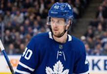Elias Pettersson Trade Rumors: Will the Canucks Deal Him to the Toronto Maple Leafs? A close-up photograph of Elias Pettersson looking off-camera, wearing an edited blue Toronto Maple Leafs home jersey with the large maple leaf crest on the chest, part of a conceptual jersey swap for trade speculation.