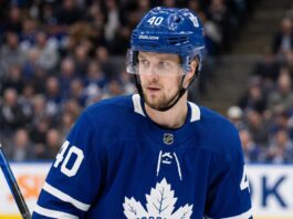 A close-up photograph of Elias Pettersson looking off-camera, wearing an edited blue Toronto Maple Leafs home jersey with the large maple leaf crest on the chest, part of a conceptual jersey swap for trade speculation.