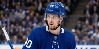 Elias Pettersson Trade Rumors: Will the Canucks Deal Him to the Toronto Maple Leafs? A close-up photograph of Elias Pettersson looking off-camera, wearing an edited blue Toronto Maple Leafs home jersey with the large maple leaf crest on the chest, part of a conceptual jersey swap for trade speculation.