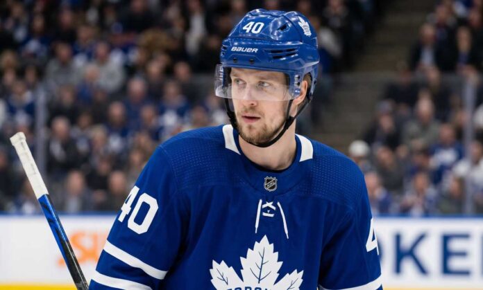 elias-pettersson-maple-leafs-trade-rumor A close-up photograph of Elias Pettersson looking off-camera, wearing an edited blue Toronto Maple Leafs home jersey with the large maple leaf crest on the chest, part of a conceptual jersey swap for trade speculation.