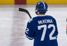 Gavin McKenna wearing a blue Toronto Maple Leafs home jersey with number 72 and the numbered blue helmet, seen from behind on an ice rink, viewed as the projected #1 overall pick for the 2026 NHL Draft.