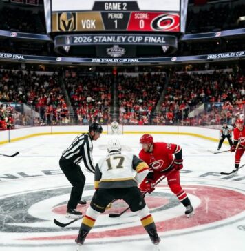 Vegas Golden Knights and Carolina Hurricanes center ice faceoff during Period 1 of the 2026 Stanley Cup Final Game 2, showing a packed arena and scoreboard.