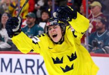 Team Sweden's Ivar Stenberg, wearing the iconic yellow and blue 'Tre Kronor' jersey with the number 15 and Svenska Spel logo, celebrating with a primal roar, raising his gloves and stick in triumph after scoring a goal during a hockey game, as San Jose Sharks fans look on in the background.