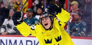 San Jose Sharks 2026 NHL Draft: Ivar Stenberg vs. Trade Scenarios Team Sweden's Ivar Stenberg, wearing the iconic yellow and blue 'Tre Kronor' jersey with the number 15 and Svenska Spel logo, celebrating with a primal roar, raising his gloves and stick in triumph after scoring a goal during a hockey game, as San Jose Sharks fans look on in the background.