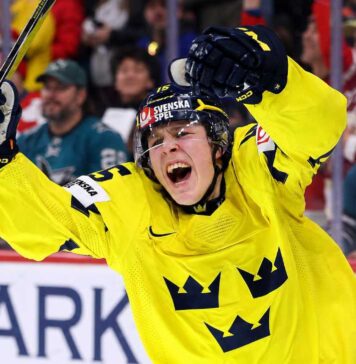San Jose Sharks 2026 NHL Draft: Ivar Stenberg vs. Trade Scenarios Team Sweden's Ivar Stenberg, wearing the iconic yellow and blue 'Tre Kronor' jersey with the number 15 and Svenska Spel logo, celebrating with a primal roar, raising his gloves and stick in triumph after scoring a goal during a hockey game, as San Jose Sharks fans look on in the background.