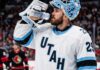 A close-up photograph of Jacob Markstrom, New Jersey Devils goaltender, wearing his white away jersey and custom mask while drinking from a water bottle on the ice, amidst trade rumors.