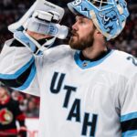Jacob Markstrom Trade Rumors: Utah Mammoth Linked to Devils Goalie A close-up photograph of Jacob Markstrom, New Jersey Devils goaltender, wearing his white away jersey and custom mask while drinking from a water bottle on the ice, amidst trade rumors.