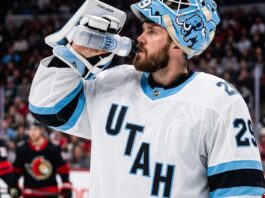 Jacob Markstrom Trade Rumors: Utah Mammoth Linked to Devils Goalie A close-up photograph of Jacob Markstrom, New Jersey Devils goaltender, wearing his white away jersey and custom mask while drinking from a water bottle on the ice, amidst trade rumors.
