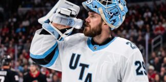 Jacob Markstrom Trade Rumors: Utah Mammoth Linked to Devils Goalie A close-up photograph of Jacob Markstrom, New Jersey Devils goaltender, wearing his white away jersey and custom mask while drinking from a water bottle on the ice, amidst trade rumors.