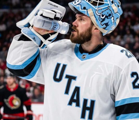 Jacob Markstrom Trade Rumors: Utah Mammoth Linked to Devils Goalie A close-up photograph of Jacob Markstrom, New Jersey Devils goaltender, wearing his white away jersey and custom mask while drinking from a water bottle on the ice, amidst trade rumors.