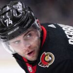 Jake DeBrusk Trade Rumors: Ottawa Senators & Vancouver Canucks Linked A close-up view visualizing Jake DeBrusk in a black Ottawa Senators hockey jersey and black helmet with the number 74.