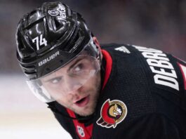 Jake DeBrusk Trade Rumors: Ottawa Senators & Vancouver Canucks Linked A close-up view visualizing Jake DeBrusk in a black Ottawa Senators hockey jersey and black helmet with the number 74.