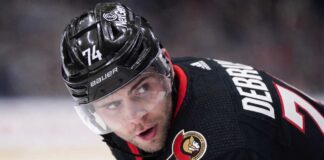 Jake DeBrusk Trade Rumors: Ottawa Senators & Vancouver Canucks Linked A close-up view visualizing Jake DeBrusk in a black Ottawa Senators hockey jersey and black helmet with the number 74.