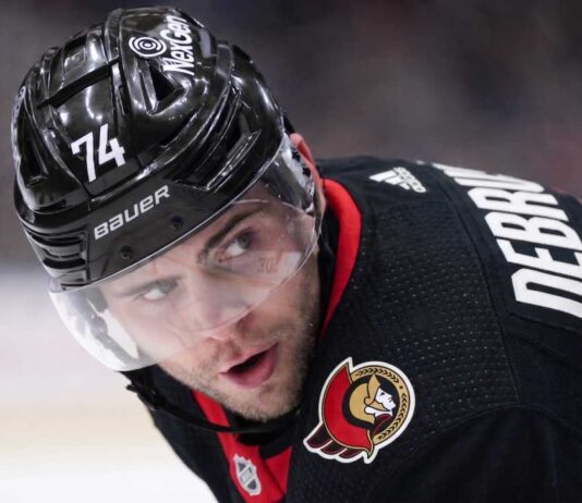 Jake DeBrusk Trade Rumors: Ottawa Senators & Vancouver Canucks Linked A close-up view visualizing Jake DeBrusk in a black Ottawa Senators hockey jersey and black helmet with the number 74.