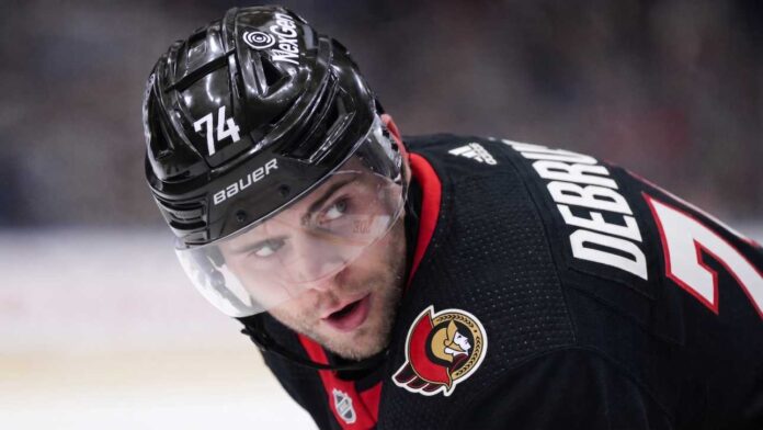 jake-debrusk-vancouver-canucks-ottawa-senators-trade A close-up view visualizing Jake DeBrusk in a black Ottawa Senators hockey jersey and black helmet with the number 74.