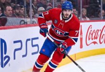 Montreal Canadiens Trade Rumors: Will Kirby Dach Be Traded? Montreal Canadiens center Kirby Dach #77 skating on the ice during an NHL game, with the PS5 and Coca-Cola logos visible on the arena boards behind him. This image relates to current trade rumors surrounding Dach.