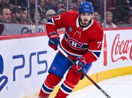 Montreal Canadiens Trade Rumors: Will Kirby Dach Be Traded? Montreal Canadiens center Kirby Dach #77 skating on the ice during an NHL game, with the PS5 and Coca-Cola logos visible on the arena boards behind him. This image relates to current trade rumors surrounding Dach.