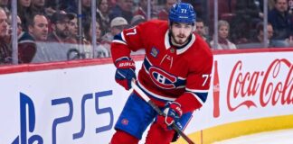 Montreal Canadiens Trade Rumors: Will Kirby Dach Be Traded? Montreal Canadiens center Kirby Dach #77 skating on the ice during an NHL game, with the PS5 and Coca-Cola logos visible on the arena boards behind him. This image relates to current trade rumors surrounding Dach.