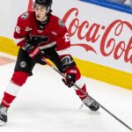 Maddox Dagenais #16 of the Quebec Remparts QMJHL, a 6'4" center, skating with the puck. Background rink boards with large Coca-Cola logo. Image from an article on Utah Mammoth NHL Draft pick analysis.