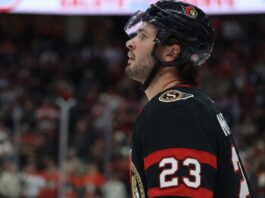 A close-up profile view of NHL hockey player Mason McTavish #23 wearing a black Ottawa Senators jersey and helmet, looking focused on the ice.