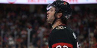 Ottawa Senators Trade Rumors: Anaheim Ducks’ Mason McTavish Linked to Sens A close-up profile view of NHL hockey player Mason McTavish #23 wearing a black Ottawa Senators jersey and helmet, looking focused on the ice.