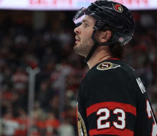 Ottawa Senators Trade Rumors: Anaheim Ducks’ Mason McTavish Linked to Sens A close-up profile view of NHL hockey player Mason McTavish #23 wearing a black Ottawa Senators jersey and helmet, looking focused on the ice.