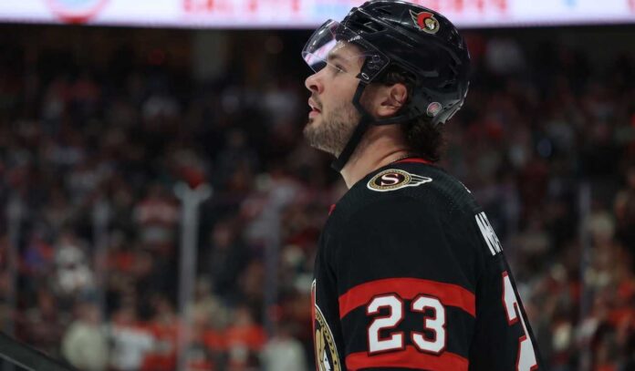 mason-mctavish-anaheim-ducks-ottawa-senators-trade A close-up profile view of NHL hockey player Mason McTavish #23 wearing a black Ottawa Senators jersey and helmet, looking focused on the ice.