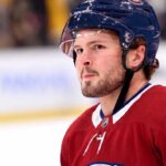 Montreal Canadiens Trade Rumors: Anaheim Ducks Mason McTavish A detailed close-up view of NHL player Mason McTavish wearing a red Montreal Canadiens (Habs) home jersey with the number 23 on the shoulder and a blue Bauer helmet with the 'CH' logo, standing on an ice rink.