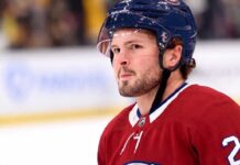 Montreal Canadiens Trade Rumors: Anaheim Ducks Mason McTavish A detailed close-up view of NHL player Mason McTavish wearing a red Montreal Canadiens (Habs) home jersey with the number 23 on the shoulder and a blue Bauer helmet with the 'CH' logo, standing on an ice rink.