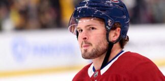 A detailed close-up view of NHL player Mason McTavish wearing a red Montreal Canadiens (Habs) home jersey with the number 23 on the shoulder and a blue Bauer helmet with the 'CH' logo, standing on an ice rink.