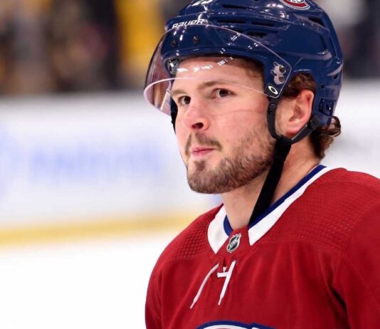 Montreal Canadiens Trade Rumors: Anaheim Ducks Mason McTavish A detailed close-up view of NHL player Mason McTavish wearing a red Montreal Canadiens (Habs) home jersey with the number 23 on the shoulder and a blue Bauer helmet with the 'CH' logo, standing on an ice rink.