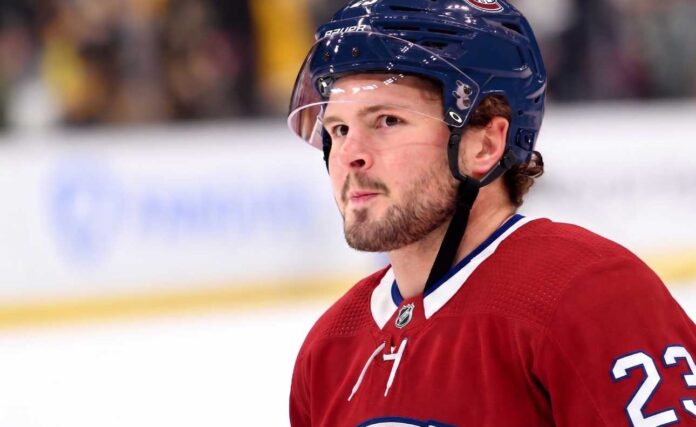 mason-mctavish-montreal-canadiens-trade A detailed close-up view of NHL player Mason McTavish wearing a red Montreal Canadiens (Habs) home jersey with the number 23 on the shoulder and a blue Bauer helmet with the 'CH' logo, standing on an ice rink.