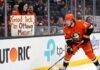 Ottawa Senators Trade Rumors: Targeting Ducks’ Mason McTavish Anaheim Ducks forward Mason McTavish skating along the boards while a fan in the stands holds a sign reading "Good luck in Ottawa Mason!" amidst Ottawa Senators trade rumors.