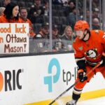 Ottawa Senators Trade Rumors: Targeting Ducks’ Mason McTavish Anaheim Ducks forward Mason McTavish skating along the boards while a fan in the stands holds a sign reading "Good luck in Ottawa Mason!" amidst Ottawa Senators trade rumors.