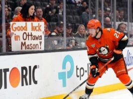 Ottawa Senators Trade Rumors: Targeting Ducks’ Mason McTavish Anaheim Ducks forward Mason McTavish skating along the boards while a fan in the stands holds a sign reading "Good luck in Ottawa Mason!" amidst Ottawa Senators trade rumors.