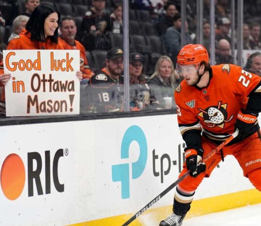Ottawa Senators Trade Rumors: Targeting Ducks’ Mason McTavish Anaheim Ducks forward Mason McTavish skating along the boards while a fan in the stands holds a sign reading "Good luck in Ottawa Mason!" amidst Ottawa Senators trade rumors.