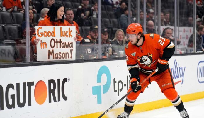 Anaheim Ducks forward Mason McTavish skating along the boards while a fan in the stands holds a sign reading "Good luck in Ottawa Mason!" amidst Ottawa Senators trade rumors.