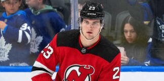 A close-up photo of hockey player Matthew Knies wearing a red New Jersey Devils home jersey, number 23, illustrative of the blockbuster trade rumor discussed in the article regarding a potential move from the Toronto Maple Leafs.