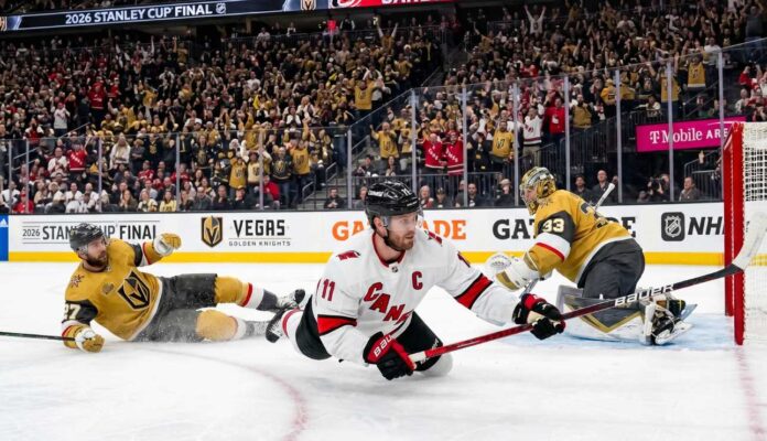nhl-news-scores-june-10-2026 Jordan Staal, wearing number 11 and a "C" on his white away jersey, falling to the ice while scoring a diving backhand goal with his Bauer stick, against the Vegas Golden Knights in Game 4 of the 2026 Stanley Cup Final. He is sliding towards the right on the ice, and the puck is visibly entering the net on the far right of the photo.