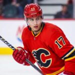 Trade Details: Calgary Flames Acquire Simon Nemec From Devils Action photograph of young right-shot defenseman Simon Nemec wearing a Calgary Flames red home jersey with number 17, holding a hockey stick on the ice.