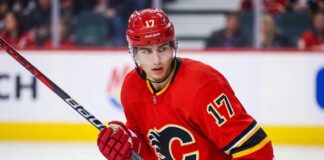 Trade Details: Calgary Flames Acquire Simon Nemec From Devils Action photograph of young right-shot defenseman Simon Nemec wearing a Calgary Flames red home jersey with number 17, holding a hockey stick on the ice.