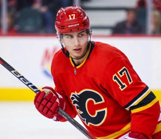 Trade Details: Calgary Flames Acquire Simon Nemec From Devils Action photograph of young right-shot defenseman Simon Nemec wearing a Calgary Flames red home jersey with number 17, holding a hockey stick on the ice.