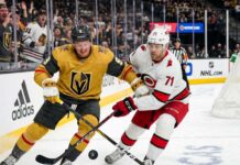 How to Watch Vegas Golden Knights vs. Carolina Hurricanes Game 1 Action shot of Vegas Golden Knights forward Jack Eichel and a Carolina Hurricanes opponent battling for the puck on the ice during Game 1 of the 2026 Stanley Cup Final, with cheering fans, NHL logos, and the 'Vegas Golden Knights' rink board in the background.