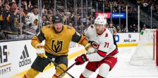 How to Watch Vegas Golden Knights vs. Carolina Hurricanes Game 1 Action shot of Vegas Golden Knights forward Jack Eichel and a Carolina Hurricanes opponent battling for the puck on the ice during Game 1 of the 2026 Stanley Cup Final, with cheering fans, NHL logos, and the 'Vegas Golden Knights' rink board in the background.