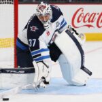 Connor Hellebuyck in Winnipeg Jets gear with Coca-Cola board ad as trade rumors link the Jets goalie to the Sabres and Hurricanes