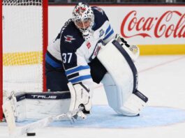 Winnipeg Jets Rumors: Will Connor Hellebuyck Be Traded After Stuart Skinner Signing? Connor Hellebuyck in Winnipeg Jets gear with Coca-Cola board ad as trade rumors link the Jets goalie to the Sabres and Hurricanes